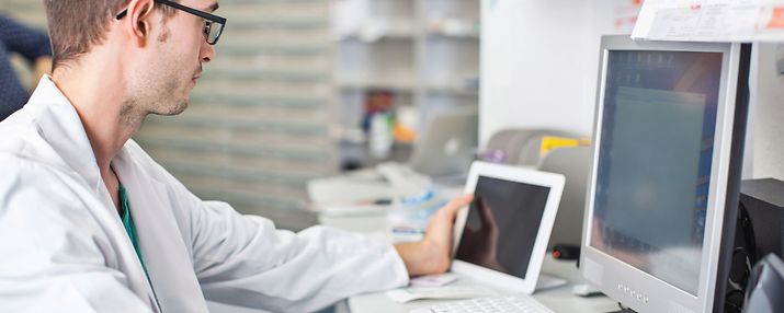 Junger Arzt betrachtet Bildschirm und Tablet